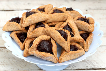 Homemade hamantaschen cookies in a serving plate on bright background with copy spce. Purim celebration concept (jewish carnaval holiday).