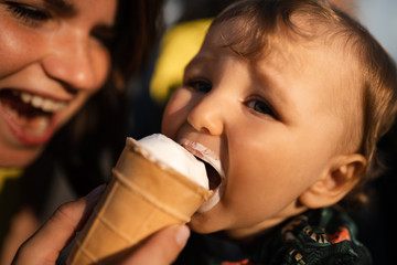 Mother feeding baby child boy ice-cream - Young mom and her baby eat white vanilla creamy dessert - Sits in a baby carriage pram - Caucasian family 1 year old