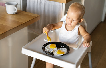 A small child independently eats a fried egg with a fork. Education and upbringing of children,...