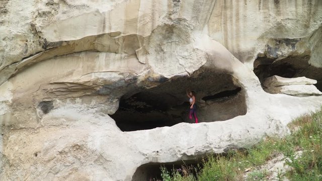 Girl traveler walks through the cavern. Cave city in the vicinity of Bakhchisarai - tope kermen. Attractions in Crimea. Slow motion. Shooting on the Steadicam