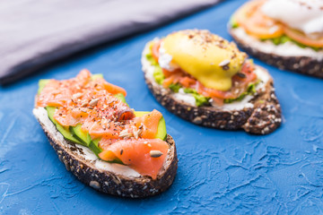 Sandwiches with smoked salmon, eggs, sauce and avocado on blue background. Concept of breakfast and healthy nutrition.