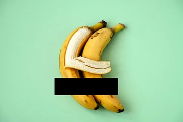 two bananas on a green background with censored black line, one banana hugs another with its peel © dvulikaia