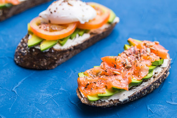 Sandwiches with smoked salmon, eggs, sauce and avocado on blue background. Concept of breakfast and healthy nutrition.