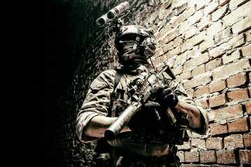 Special operations forces soldier, counter terrorism assault team fighter with night vision device on helmet and service rifle, low key indoor shot brick wall