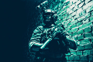Obraz na płótnie Canvas Special operations forces soldier, counter terrorism assault team fighter with night vision device on helmet and service rifle, low key indoor shot brick wall