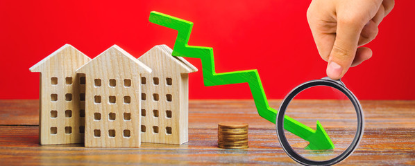 Miniature wooden houses and a green arrow down. The concept of low cost real estate. Lower mortgage...