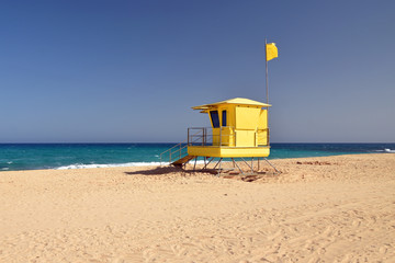 Bright yellow lifeguard station on beach. Sunny day, blue sky, turquoise water. Corralejo, Fuerteventura, Spain.