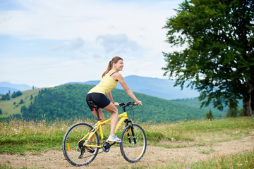 Fototapeta na wymiar Athlete happy woman cyclist cycling on yellow mountain bike, enjoying summer day in the mountains. Outdoor sport activity, lifestyle concept