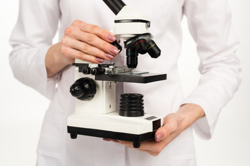 cropped view of scientist in white coat holding microscope isolated on white