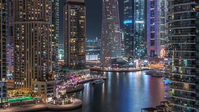 Aerial view of Dubai Marina residential and office skyscrapers with waterfront with palms night timelapse. Floating boats and yachts