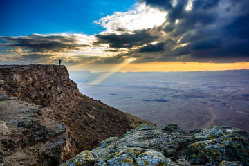 Fototapeta na wymiar Man on a desert cliff, with sun breaking through clouds, Negev Desert