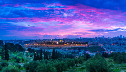 Obraz premium Dramatyczny fioletowo-różowy zachód słońca nad Starym Miastem w Jerozolimie: Kopuła na Skale, Złota / Mercy Gate i St Stephen's / Lions Gate; panoramiczny widok z Góry Oliwnej z drzewami oliwnymi na pierwszym planie