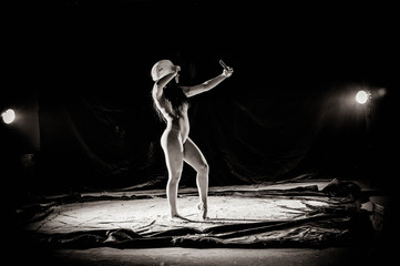 The girl with the flour on the body stretches the arms up with thrown flour on black background black and white image