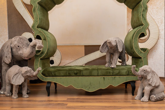 Group of gray plush elephants standing on green sofa. Photo setting ready for taking photo of children in indoor playground.