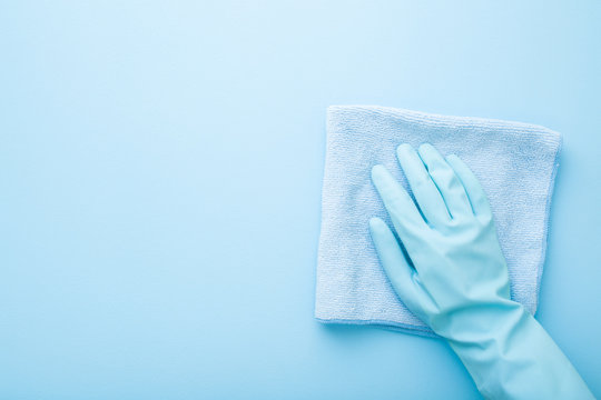 Hand In Rubber Protective Glove Wiping Table, Wall Or Floor Surface In Kitchen, Bathroom Or Other Room. Closeup. Empty Place For Text Or Logo. Light Pastel Blue Background. Top Down View.