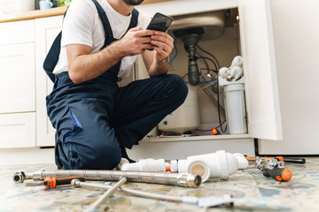 Man plumber work in uniform indoors using mobile phone.