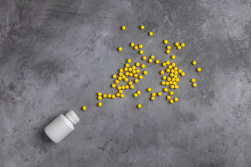 Yellow vitamins poured from a white can on a gray concrete background.