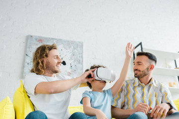 happy homosexual parents near mixed race son in virtual reality headset