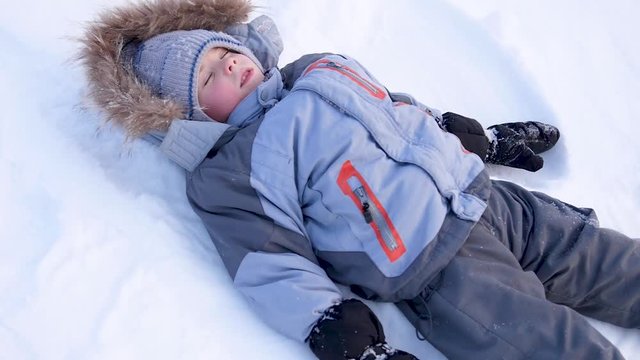 the baby lies on snow and making a snow angel in slowmotion
