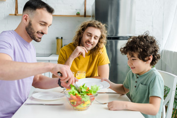 happy homosexual men and mixed race kid looking at tasty salad