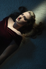 Dead woman with blonde hair in red dress on white carpet.