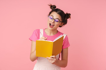 Photo of excited charming girl in eyeglasses writing in exercise book
