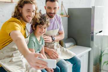 selective focus of happy homosexual parents taking selfie with mixed race son