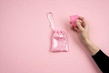 Isolated hand holding a vaginal bowl on a pink background.