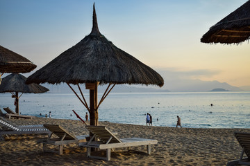 Straw umbrellas on a sandy beach at dawn and wooden deck chairs by sea