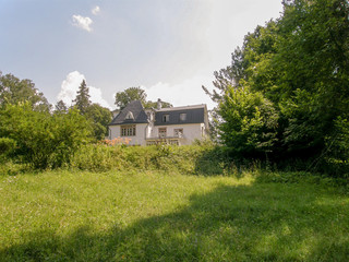 Obraz premium A white house with a black roof behind green bushes and trees against a blue sky
