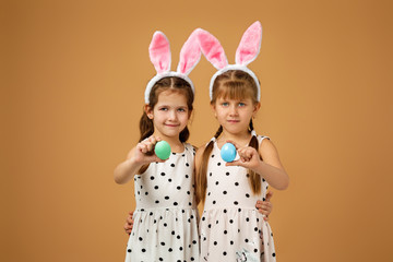 Obraz na płótnie Canvas happy cute little child girls with pink bunny ears holding painted Easter eggs on studio yellow background. Easter day