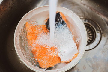 Water pouring over plastic bowl containing two pieces of fresh bio organic salmon fish
