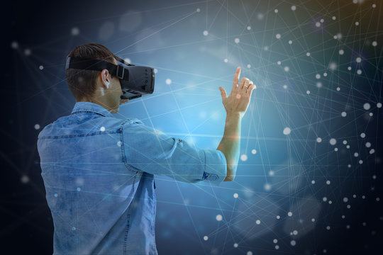 Beautiful young man using VR helmet while touching air in colorful neon lights. Guy in glasses of virtual reality with blue backlight over dark magic universe background.