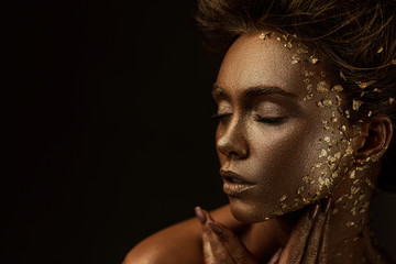 Fashion art portrait of model girl with holiday golden shiny professional makeup. beaty woman with gold metallic body and hair on dark background. Gold glowing skin. copy space