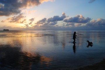 Fototapeta premium Beautiful sunset in the Northern Mariana Islands with the silhoutte of a woman and a dog in the beach