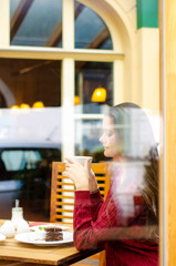 Woman sitting with cup of tea inside cafe, view through the window