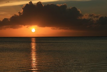 Dramatic clouds above a full round setting sun reflected in the sea