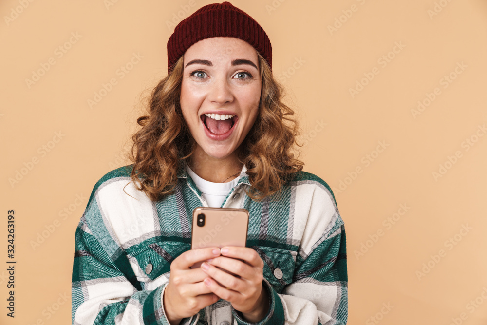 Poster Photo of nice excited woman in knit hat smiling and using cellphone