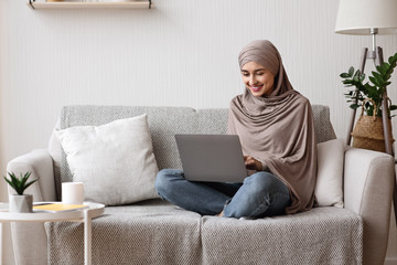 Modern arab girl in hijab using laptop at home, working remotely