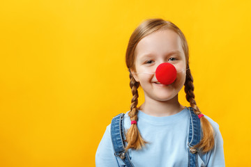 Happy funny child clown with a red nose. Cheerful little girl on a yellow background. April 1st...