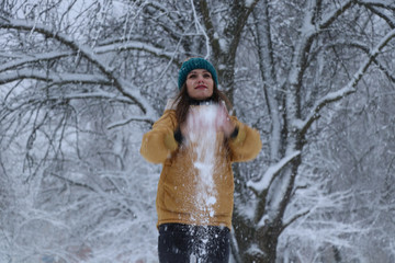 Fototapeta premium Beautiful girl in a yellow jacket, jeans and a green hat on the snow. Snowy weather, everything in the snow is white. Snowflakes.