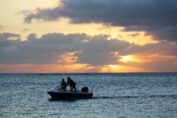 Silhouette of fishermen in a boat sailing at sunset.