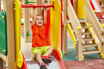Fototapeta na wymiar funny little boy on playground. playing child on slide.