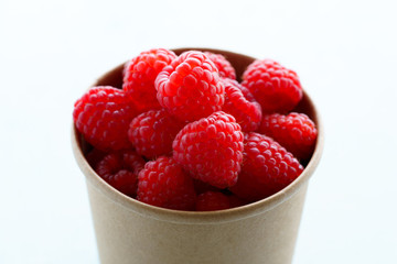 Freshly picked organic raspberries in recycled paper cup. High resolution, white background
