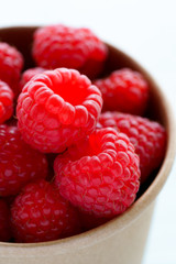 Freshly picked organic raspberries in recycled paper cup. High resolution, white background