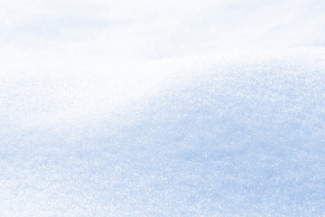 Background of sparkling fresh white snow texture with light blue sky reflection tone.