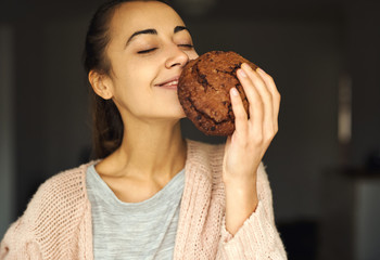 pretty smiling woman holding and sniffing huge chocolate cookie with pleasure. food, sweets and bakery concept.