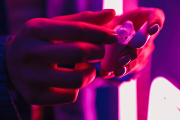 Woman posing over neon lights holding wireless earphones