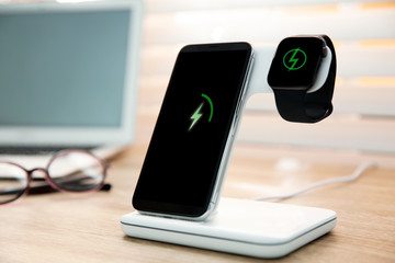Mobile phone and smartwatch with wireless charger on wooden table. Modern workplace accessory