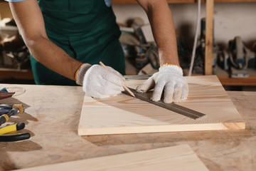 Professional carpenter measuring wooden board in workshop, closeup